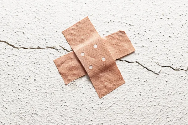 band-aid plaster in cross shape on a crack in the wall, concept for botched construction and doctoring around symptoms, copy space