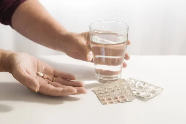 female hands take pills and a glass of water, blister pack on the white table, light background with copy space, selected focus, narrow depth of field