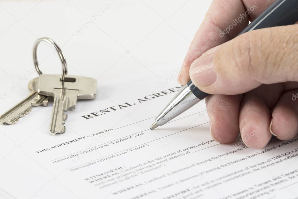 hand is writing with a pen on a rental agreement document, house keys in the background, selected focus, narrow depth of field