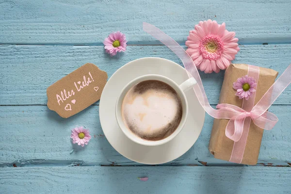 Taza de café, flores rosadas y un regalo en el fondo de madera azul pastel —  Fotos de Stock