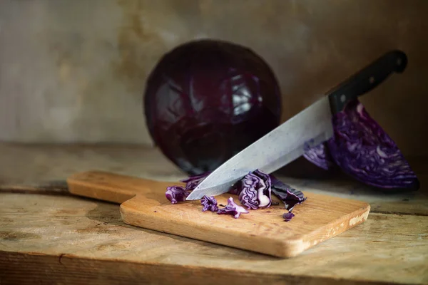 red cabbage is cut with a large kitchen knife on a kitchen board on a rustic wooden table, copy space, selected focus, narrow depth of field