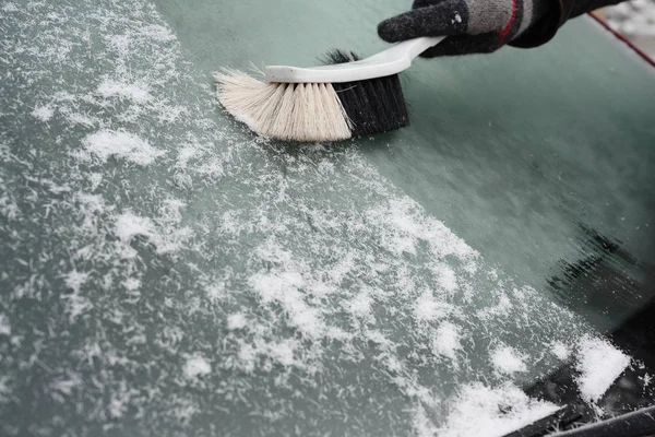 hand broom sweeps the snow from the windshield of a car in winter, copy space, selected focus