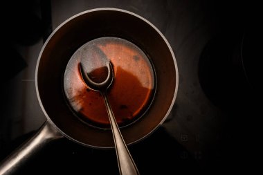 pot and spoon with beef stock while cooking a red wine morel sauce on a black stove, dark background with copy space, high angle view from above, selected focus clipart