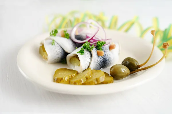 Rollmops or rolled pickled herring with red onions, gherkins and capers on a white table with party streamer, a traditional sour hangover breakfast — Stock Photo, Image