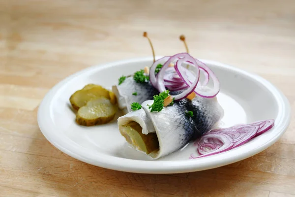 Fregonas o arenque en escabeche enrollado con cebollas rojas, pepinillos y alcaparras, un desayuno con resaca agria, por ejemplo, el miércoles de ceniza en una mesa de madera, espacio para copiar — Foto de Stock