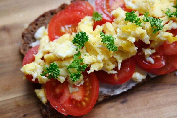 Vollkornbrot mit Tomaten, Rührei und Petersiliengarnitur auf einem Holzbrett, von oben gesehen — Stockfoto