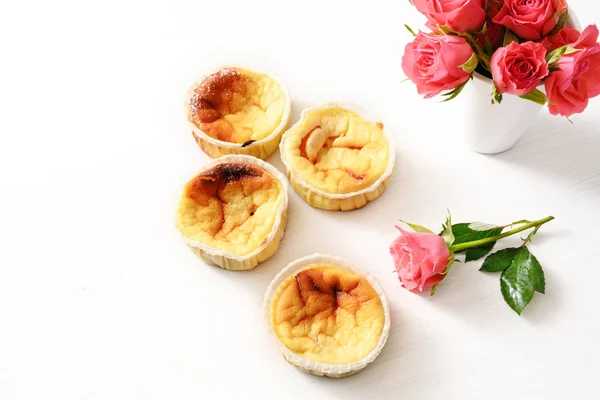 Hemmagjord små ostmassa kakor eller muffins och rosa rosor på ett vitt bord med kopia utrymme, bakgrunden bleknar till vitt — Stockfoto