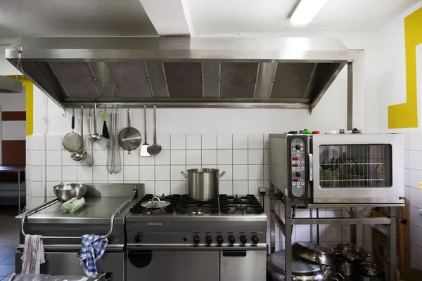 Sistema de cocina de acero inoxidable con estufa, parrilla, horno y campana extractora en una cocina comedor profesional —  Fotos de Stock