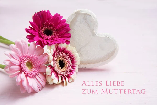 Flores cor-de-rosa e um coração de madeira pintado de branco em um fundo de cor pastel, texto alemão Alles Liebe zum Muttertag, significando All Love for Mother 's Day — Fotografia de Stock