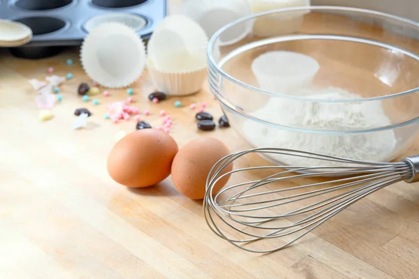 Schneebesen, Eier, Mehl und Muffinform zum Cupcake-Backen auf einem Holztisch, Kopierraum — Stockfoto