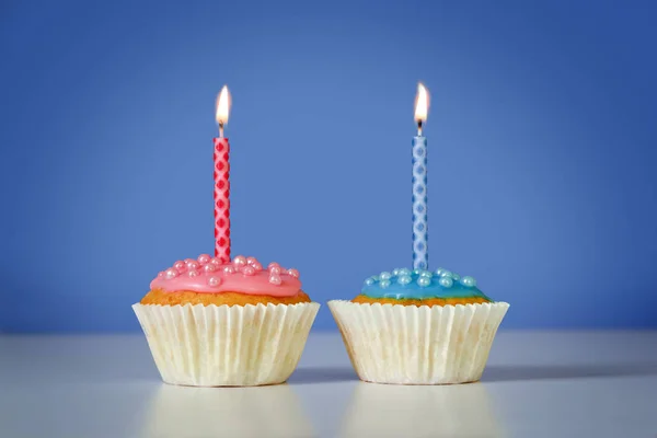 Dos magdalenas o cupcakes con velas ardientes de color rosa y azul sobre un fondo azul, concepto de cumpleaños con espacio para copiar — Foto de Stock