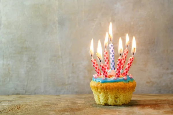 birthday muffin or cupcake with red and blue burning candles on a wooden board against a rustic wall, copy space