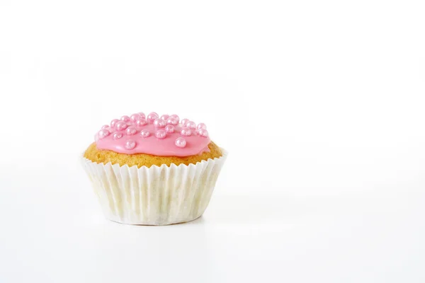 Magdalena con glaseado rosa y perlas de azúcar en una taza de papel sobre fondo gris claro se desvanece a blanco, espacio de copia — Foto de Stock