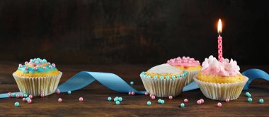 pembe ve mavi dekore muffins veya cupcakes bir kurdele ve koyu kahverengi bir arka plan, kopya alanı ile panoramik biçimi ne karşı rustik ahşap tahta üzerinde yanan bir mum ile