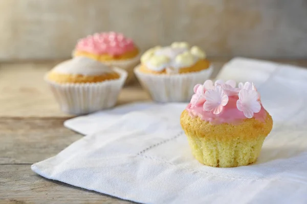 Magdalenas o cupcakes con glaseado rosa y decoración de flores en una servilleta blanca y una tabla de madera rústica, espacio para copiar — Foto de Stock