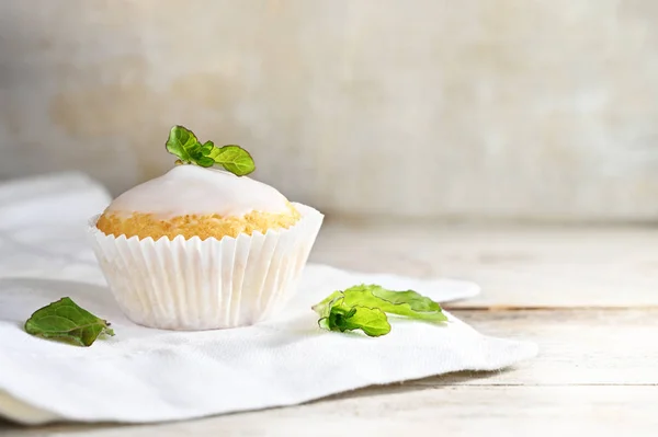 Muffin lub Cupcake z białym lukier i mięta dekorować na serwetce drewniany stół przed światłem rustykalnym tle, Kopiuj przestrzeń — Zdjęcie stockowe