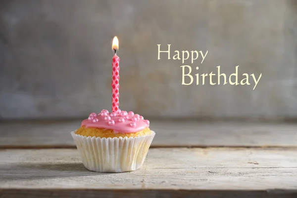 Magdalena o magdalena con una vela ardiente rosa sobre un tablero de madera sobre un fondo rústico, texto Feliz cumpleaños, concepto de tarjeta de felicitación — Foto de Stock