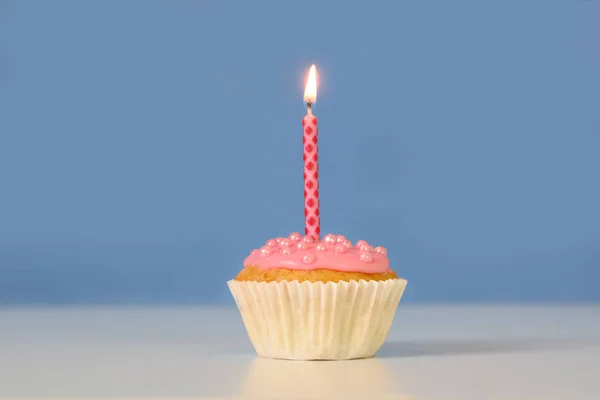 Muffin o cupcake con una candela rosa accesa su uno sfondo blu, concetto di compleanno con ampio spazio di copia — Foto Stock