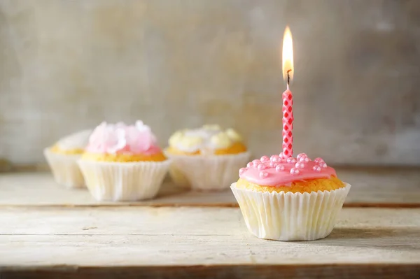 Magdalenas o cupcakes con una vela ardiente rosa sobre una tabla de madera sobre un fondo rústico, concepto de cumpleaños con espacio para copiar — Foto de Stock