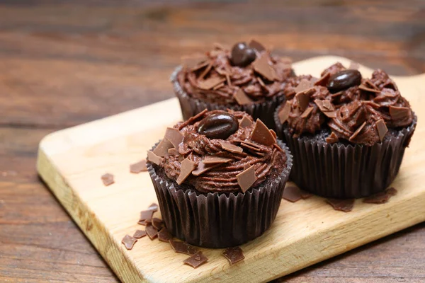 Magdalenas marrones con crema de manteca de cacao, decoradas con chips de chocolate y granos de café en una pizarra de madera rústica, espacio para copiar — Foto de Stock