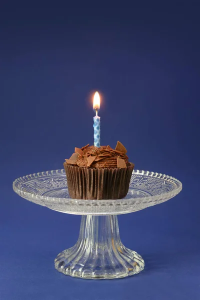 ガラスのボウルに燃えるキャンドルを持つチョコレートカップケーキ、コピースペース付きの青い背景、誕生日のコンセプト — ストック写真