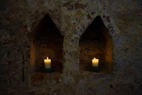 Two white burning candles in two niches in a dark old brick wall of a monastery, copy space — Stock Photo, Image