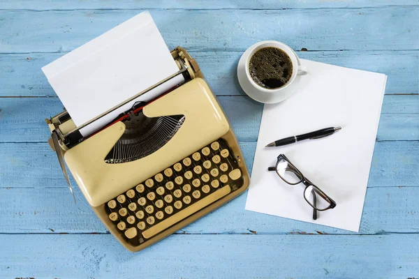 Old beige typewriter from the 1950s with paper, coffee and glasses on a blue painted wooden table, high angle view from above — Stock Photo, Image