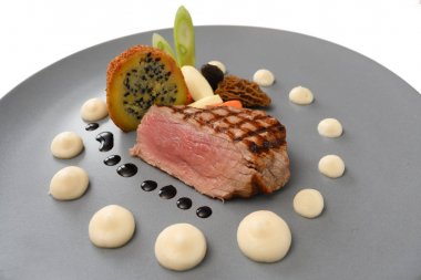 Kavrulmuş dana eti, morels, sebze ve kızarmış patates soğan tohumları ile doldurulmuş mavi gri plaka üzerinde hizmet