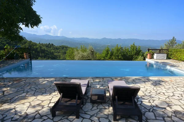 Cadeiras confortáveis na piscina em frente a uma ampla paisagem montanhosa com céu azul, espaço de cópia — Fotografia de Stock