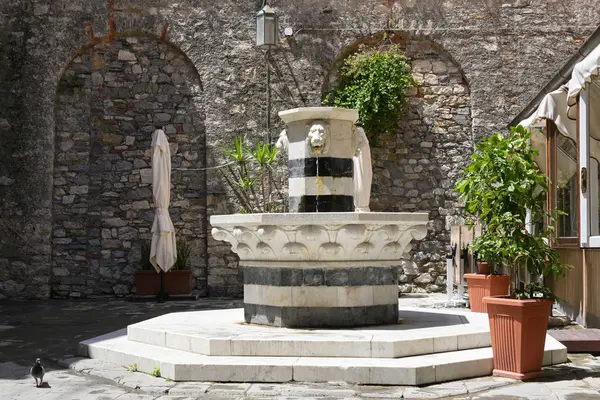 Fuente de agua potable de mármol con cabezas de león en una plaza en el casco antiguo de porto venere, liguria, italia — Foto de Stock