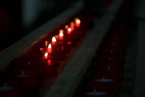 Velas rojas ardientes votivas o de oración en un estante en una vieja iglesia oscura en Italia, espacio para copiar —  Fotos de Stock