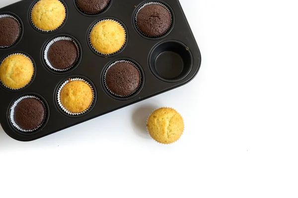 Pastelitos recién horneados en dos variedades en una lata de magdalenas, uno de pie fuera, fondo de esquina se desvaneció a blanco, espacio de copia, vista de ángulo alto desde arriba — Foto de Stock