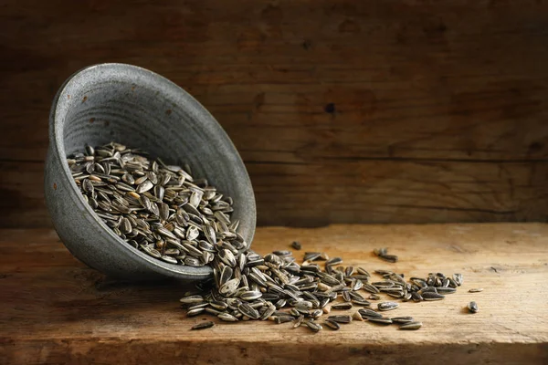 Семена подсолнечника, популярный корм для птиц для зимнего кормления, высыпание из чаши на деревенскую деревянную доску, пространство для копирования — стоковое фото