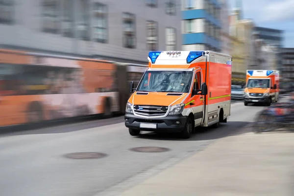 Dos ambulancias de emergencia están conduciendo rápido con luz intermitente azul a través de la ciudad, tiro panorámico con desenfoque de movimiento —  Fotos de Stock