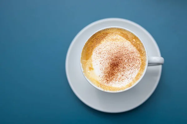 Cup of cappuccino with cocoa powder on a blue background, view directly from above, copy space — Stock Photo, Image