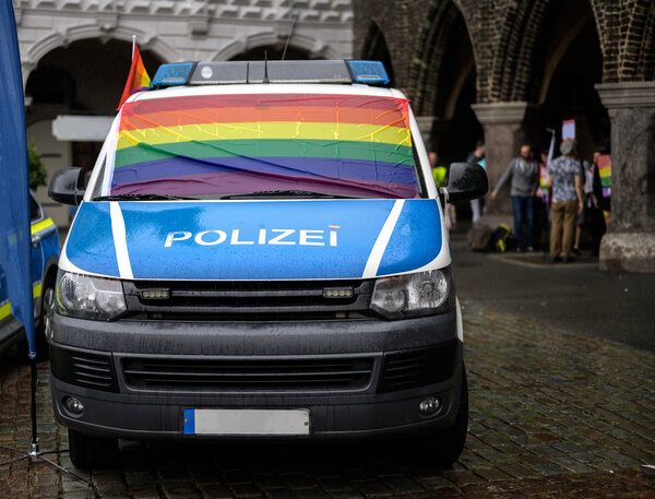 police car with a wet rainbow flag on the windshield at the rainy christopher street day 2019 in luebeck, germany, german text on the car Polizei means police