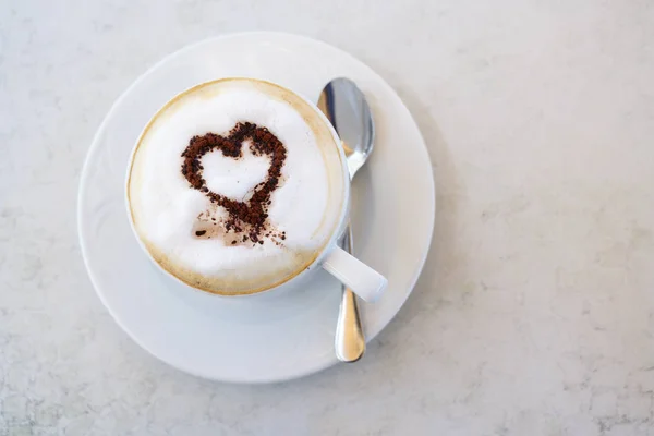 Cup of cappuccino with cocoa powder in heart shape on a table in a street cafe, high angle view from above, copy space, selected focus, narrow depth of field — Stock Photo, Image