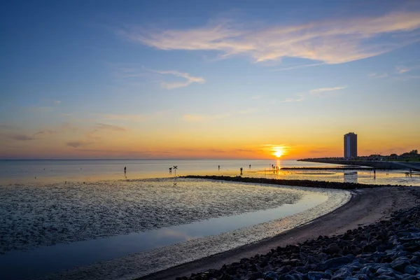 Strand und Wolkenkratzer von Büsum an der Nordsee bei Ebbe bei Sonnenuntergang, einige Touristen als Silhouetten im Wattenmeer in Deutschland, Kopierraum — Stockfoto