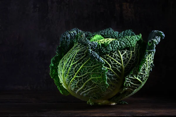 Varză verde savoy, o legumă sănătoasă de iarnă în lumină dramatică pe lemn rustic întunecat și moody cu spațiu de copiere — Fotografie, imagine de stoc