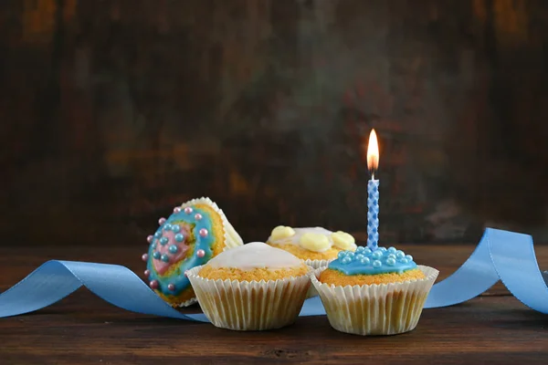 복사 공간이있는 어두운 갈색 배경에 대한 소박한 나무 보드에 파란색 리본과 불타는 촛불로 머핀이나 컵 케이크를 장식 — 스톡 사진