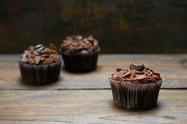 Tres cupcakes de chocolate con crema de manteca de cacao en madera oscura, uno está en foco, espacio de copia — Foto de Stock