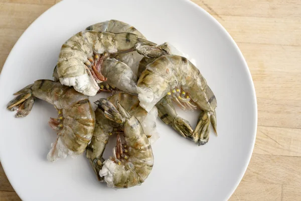 Raw black tiger prawn shrimps without head, cooking ingredients for a tasty dish on a white plate and a wooden kitchen worktop, high angle view from above — Stock Photo, Image