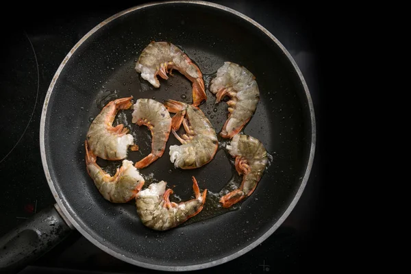 Juicy fresh black tiger prawn shrimps are roasted in a black pan on the stove, cooking a tasty meal for low carb diet, high angle view from above — Stock Photo, Image