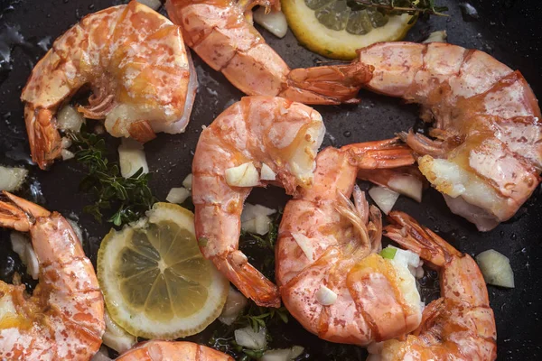 Roasted tiger prawn shrimps with garlic, lemon and herbs in a black pan, cooking background, high angle view from above — Stock Photo, Image