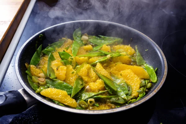 Сахарный горошек, оранжевые ломтики и весенний лук жареный в паровой кастрюле, приготовление здоровой вегетарианской пищи для низкоуглеводной овощной еды — стоковое фото