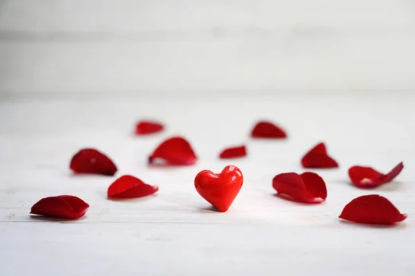 Coração de vidro vermelho entre pétalas de rosa em um fundo de madeira cinza claro, conceito de amor com espaço de cópia — Fotografia de Stock