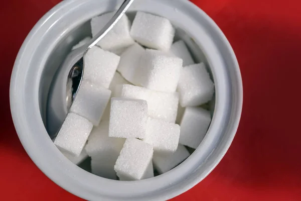 Cubes de sucre et cuillère dans un bol blanc sur fond rouge, vue grand angle d'en haut — Photo