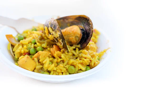 Gran mejillón en una porción de paella, comida callejera española de arroz y mariscos en un tazón de cartón sostenible y un tenedor de madera, fondo con espacio de copia se desvanece a blanco, tiro de cerca — Foto de Stock