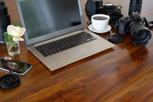 Lugar de trabajo del fotógrafo con computadora portátil, cámara, lentes, taza de café y teléfono en una mesa de madera, espacio para copiar — Foto de Stock
