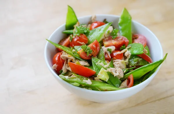 Pois mange-tout et tomates cerises au thon comme salade saine pour un régime pauvre en glucides dans un bol blanc sur une table en bois, espace de copie — Photo